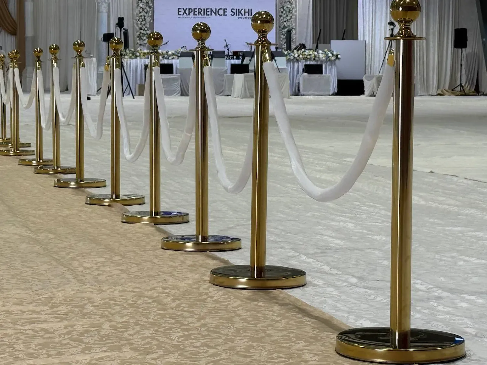 Gold rope stanchions with white velvet ropes along a ballroom aisle